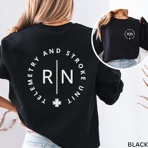 May include: Black sweatshirt with a white circular graphic on the back that reads "Telemetry and Stroke Unit" around the letters "RN" with a cross symbol. A smaller version of the graphic is on the front. The word "BLACK" is at the bottom.