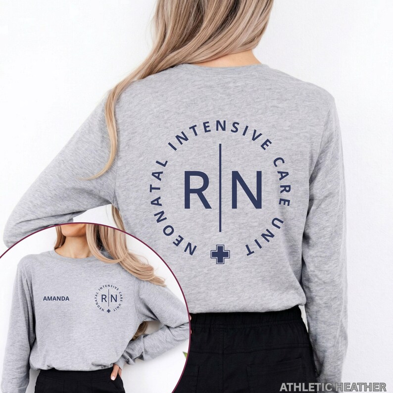 May include: A heather gray long-sleeve shirt featuring a dark blue circular graphic on the back with the text NEONATAL INTENSIVE CARE UNIT and RN in the center. The front left chest displays the name AMANDA and a smaller version of the same graphic.