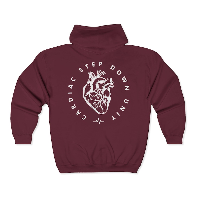 Op de afbeelding: Een bordeauxrode hoodie met ritssluiting. De achterkant heeft een witte cirkelvormige afbeelding met een anatomische hartillustratie, de woorden "CARDIAC STEP DOWN UNIT" en een hartslaglijn. De hoodie heeft een capuchon.