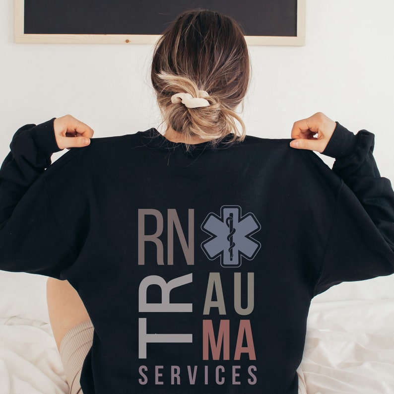 Puede incluir: Sudadera negra con el texto "RN Trauma Services" en un dise&ntilde;o vertical apilado. Un s&iacute;mbolo m&eacute;dico estilizado con una serpiente y un bast&oacute;n est&aacute; centrado sobre el texto.
