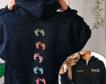 May include: A black zip-up hoodie featuring a vertical row of five pairs of baby footprints in muted colors on the back. The front displays the text "Amanda RN" and "NICU nurse" in multi-colored lettering on the chest area.