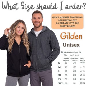 Op de afbeelding: Een man en een vrouw dragen een zwarte en een antracietgrijze hoodie met rits. De afbeelding bevat de tekst "Welke maat moet ik bestellen?" en een maattabel met afmetingen in inches voor de "Gilden Unisex" hoodie.