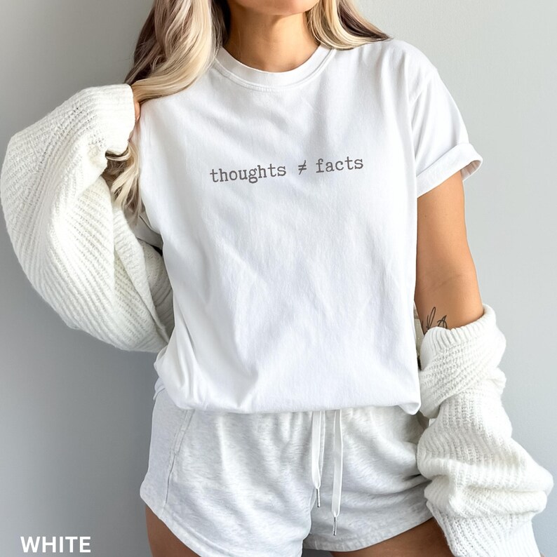 Puede incluir: Camiseta blanca con la frase "thoughts &ne; facts" impresa en gris oscuro. La camiseta forma parte de un conjunto a juego con pantalones cortos blancos. Un su&eacute;ter blanco est&aacute; sobre los hombros.
