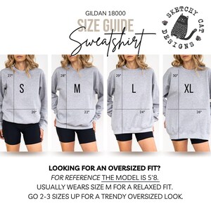 Op de afbeelding: Een Gildan 18000 sweatshirt maattabel met vier grijze sweatshirts in de maten S, M, L en XL. Elke afbeelding toont lengte- en breedtematen in inches. De tekst bevat 'Sketchy Cat Designs', 'Looking for an oversized fit?' en modelinformatie.