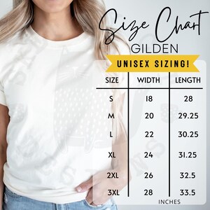 Pode incluir: Uma camiseta creme com um desenho de gato branco. &Eacute; exibida uma tabela de tamanhos, mostrando as medidas em polegadas para os tamanhos S a 3XL. A tabela inclui as dimens&otilde;es de largura e comprimento para cada tamanho.