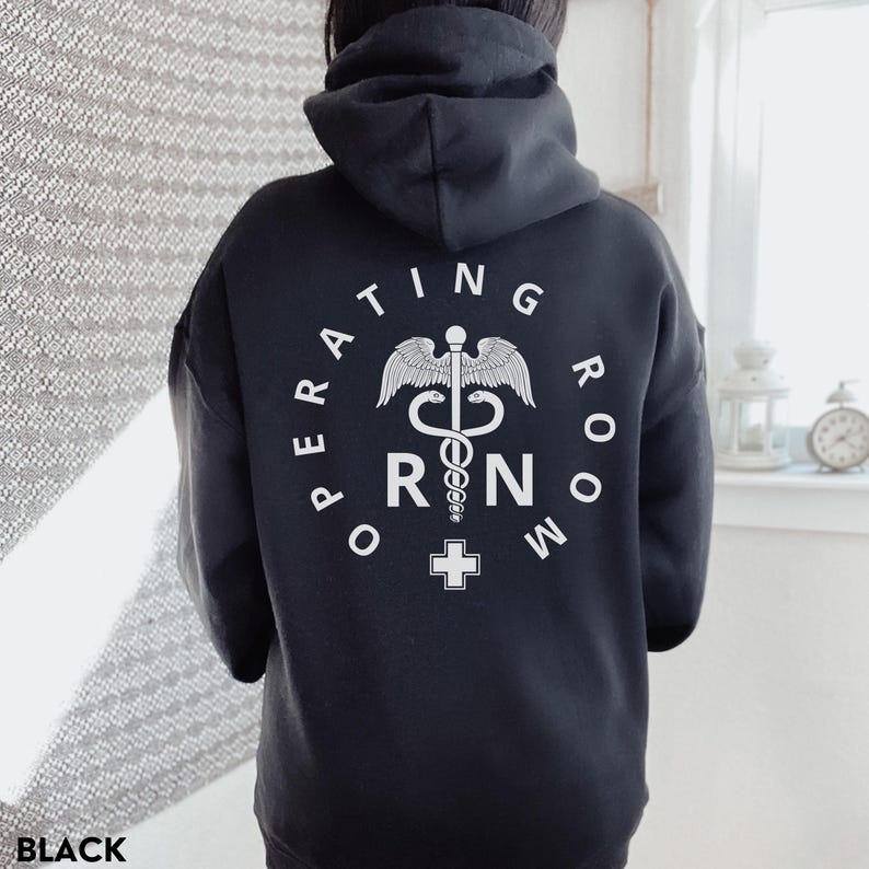 Puede incluir: Sudadera con capucha negra con un gr&aacute;fico blanco de un caduceo y el texto "Operating Room RN".