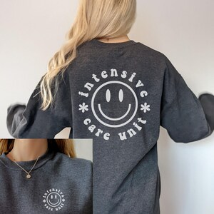 May include: A dark gray sweatshirt with a white smiley face graphic and the text "*intensive care unit*" around the smiley face.