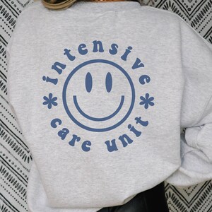 May include: Gray sweatshirt with a blue graphic of a smiley face and the text "*intensive care unit*"
