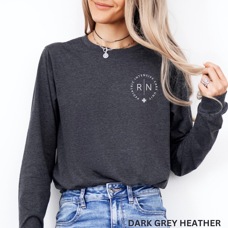 Puede incluir: Camiseta de manga larga en gris oscuro jaspeado con un gr&aacute;fico circular blanco que dice "Pediatric Intensive Care Unit RN".