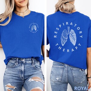 Pode incluir: Camiseta azul royal com texto branco e um gr&aacute;fico de pulm&otilde;es. A frente da camiseta tem um pequeno gr&aacute;fico de pulm&otilde;es com as palavras "Respiratory Therapy" em um c&iacute;rculo. A parte de tr&aacute;s da camiseta tem um gr&aacute;fico de pulm&otilde;es maior com o mesmo texto.