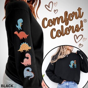 May include: Black long-sleeve shirt with colorful dinosaur graphics on the left sleeve. The shirt features the text "Comfort Colors!" and a small dinosaur graphic with the word "PEDS" on the chest. The shirt is a comfortable, casual style.
