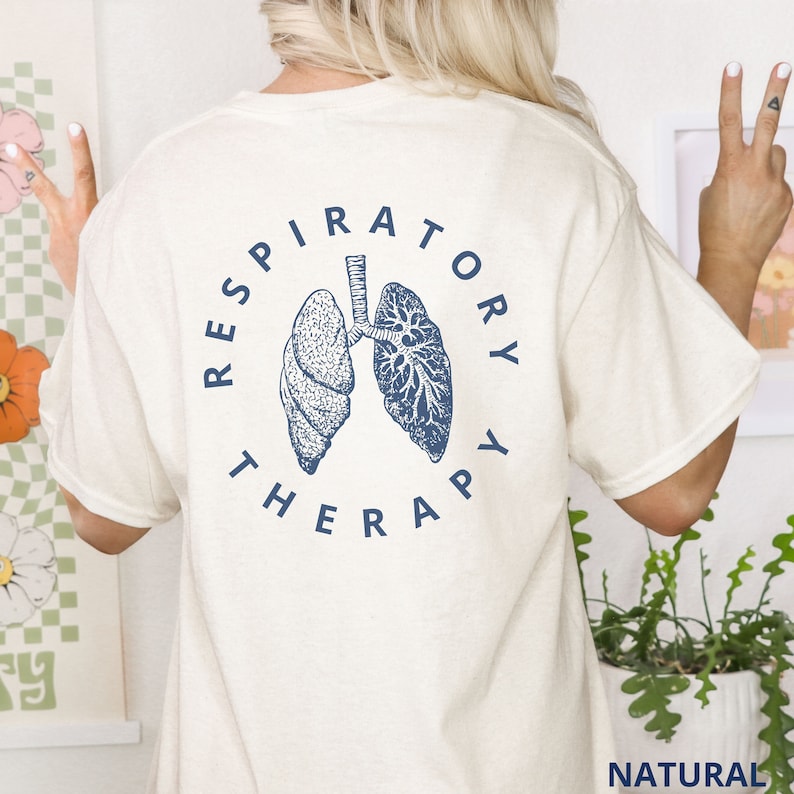 Pode incluir: Camiseta creme com uma ilustra&ccedil;&atilde;o azul marinho dos pulm&otilde;es e as palavras "RESPIRATORY THERAPY" em um design circular. A camiseta &eacute; feita de um material macio e tem um corte folgado.