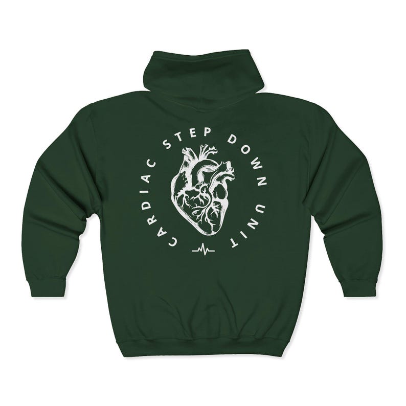 Op de afbeelding: Een donkergroene hoodie met ritssluiting en een witte afbeelding op de rug. De afbeelding toont een gestileerd menselijk hart in een cirkel met de woorden "CARDIAC STEP DOWN UNIT" en een hartslaglijn.