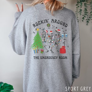 Op de afbeelding: Een grijs gem&ecirc;leerd sweatshirt met een afbeelding op de achterkant van drie skeletten met kerstmutsen, een kerstboom, een discobal en medische apparatuur. De tekst luidt ROCKIN' AROUND THE EMERGENCY ROOM in zwarte letters.