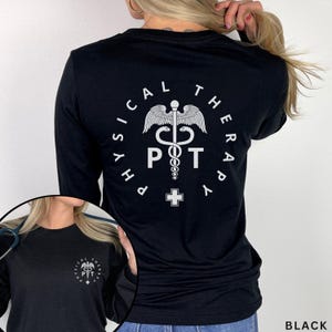 May include: A black long-sleeve shirt featuring a white graphic on the back and a smaller matching graphic on the front left chest. The design includes the text PHYSICAL THERAPY, the letters PT, a caduceus symbol, and a small medical cross icon.