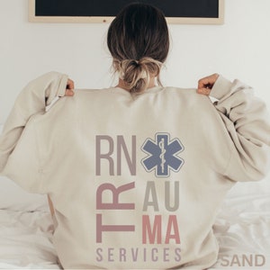 Puede incluir: Una sudadera beige con el texto "RN Trauma Services" y una estrella m&eacute;dica azul con una serpiente dentro.