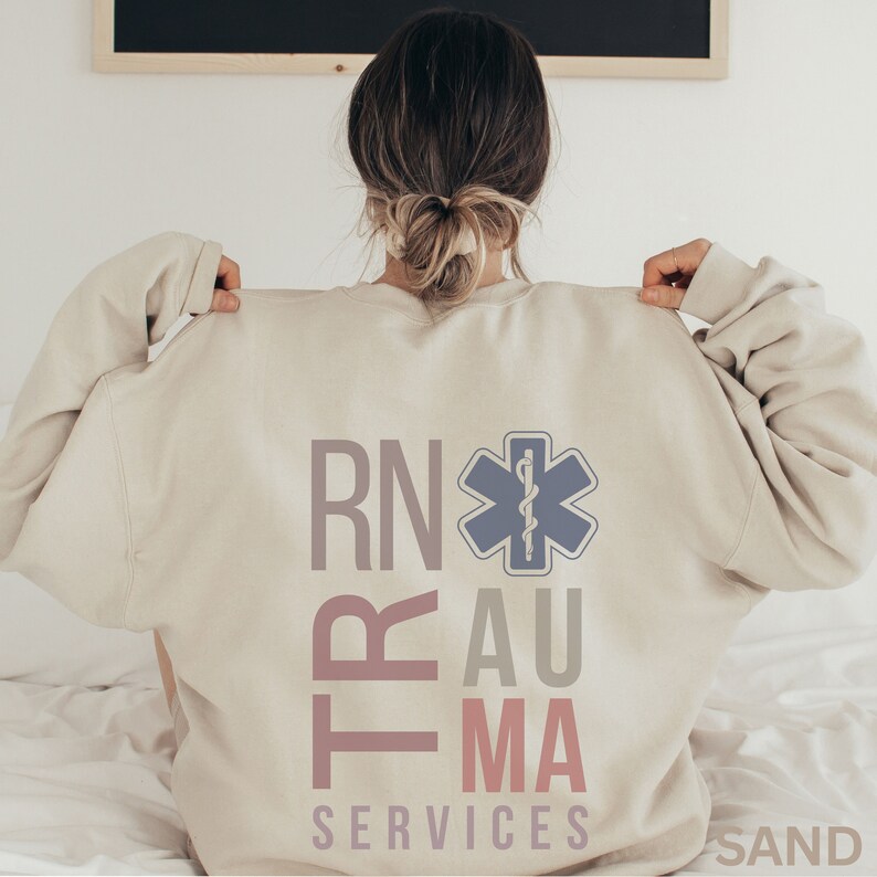 Puede incluir: Una sudadera beige con el texto "RN Trauma Services" y una estrella m&eacute;dica azul con una serpiente dentro.