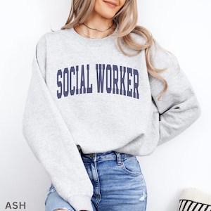 Peut inclure: Sweat-shirt gris clair avec l'inscription "SOCIAL WORKER" en lettres majuscules bleu marine. Le sweat-shirt est de style col rond et est fait d'une matière douce. Le mot "ASH" est imprimé en bas à gauche.