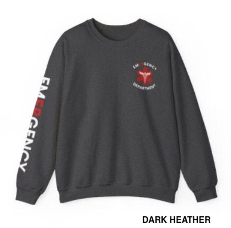May include: Dark heather grey sweatshirt with the words "EMERGENCY DEPARTMENT" and a red medical symbol on the front. The words "EMERGENCY" are printed vertically on the left sleeve in white.