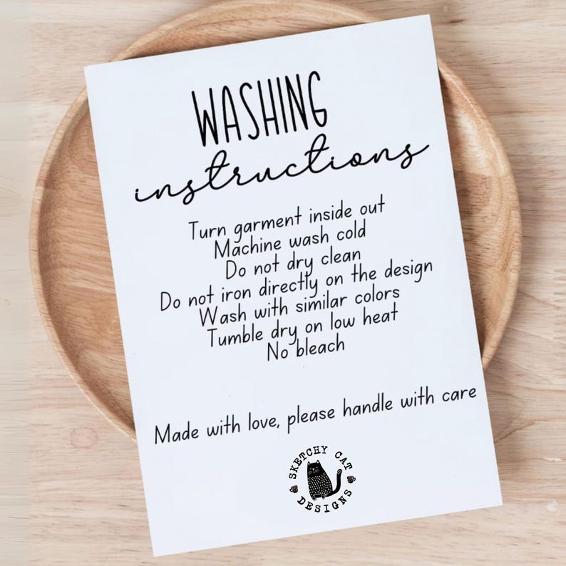 May include: A white card with black text reading "WASHING instructions" and care instructions. The card includes a "Sketchy Cat Designs" logo and is placed on a wooden plate.