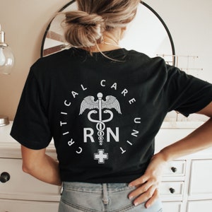 May include: Black t-shirt with a white graphic of a medical symbol, a snake wrapped around a staff with wings, and the text "CRITICAL CARE UNIT RN".