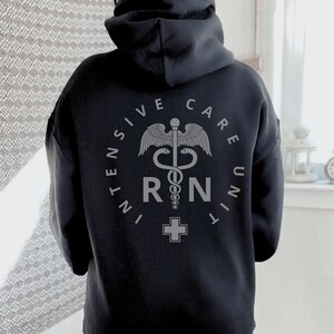 Peut inclure: Sweat-shirt &agrave; capuche noir avec un graphique gris d'un caduc&eacute;e m&eacute;dical et le texte "INTENSIVE CARE UNIT RN".