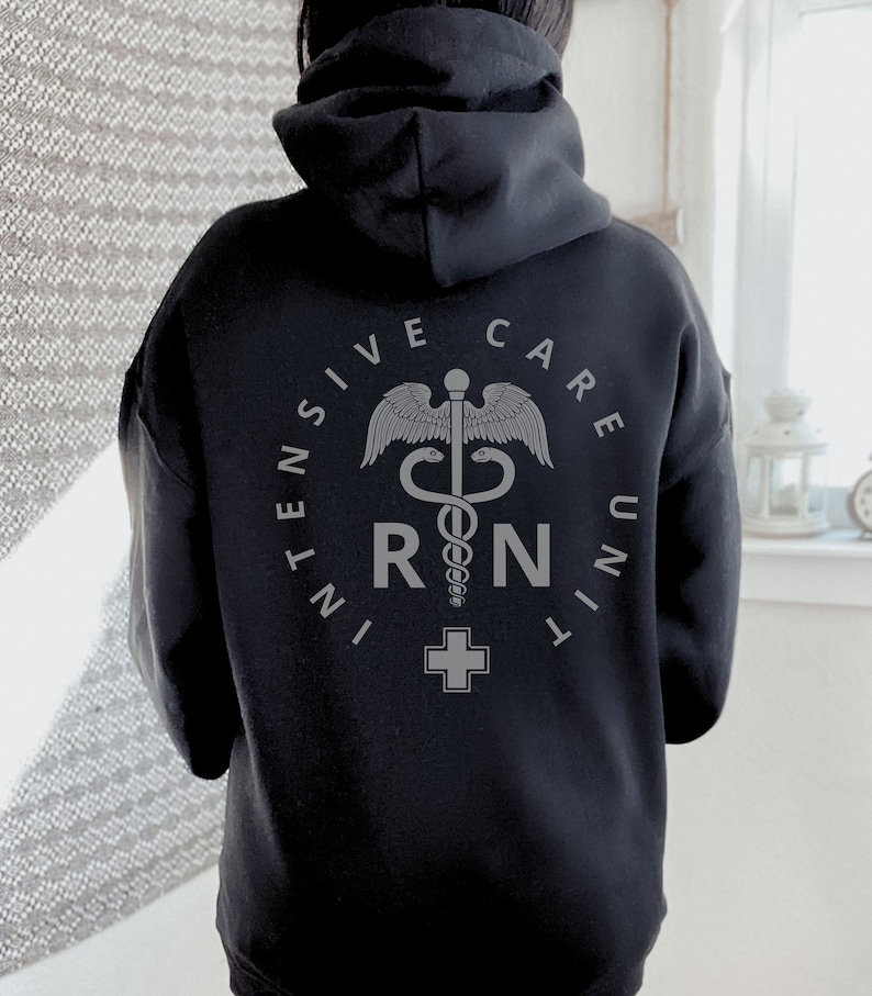 Peut inclure: Sweat-shirt &agrave; capuche noir avec un graphique gris d'un caduc&eacute;e m&eacute;dical et le texte "INTENSIVE CARE UNIT RN".