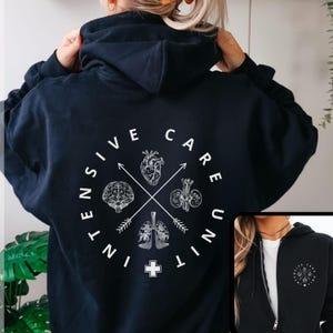 Peut inclure: Un sweat à capuche bleu marine avec un motif blanc au dos. Le motif présente un cercle avec les mots "Intensive Care Unit" et des illustrations du cœur, du cerveau, des poumons et des reins. Une petite image montre une version zippée.