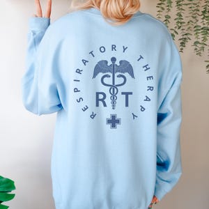 May include: Light blue sweatshirt with a graphic of a medical caduceus and the text "Respiratory Therapy RT" in a circle.