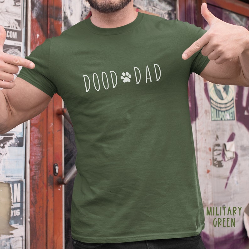 May include: Military green t-shirt with the text "DOOD DAD" in white, featuring a paw print graphic. The shirt is a solid color and has a crew neck.