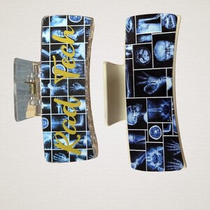 May include: Two rectangular hair claw clips featuring a grid pattern of various blue and white medical X-ray images. One clip displays the gold cursive text Rad Tech vertically across the center, while the other shows only the X-ray grid pattern.