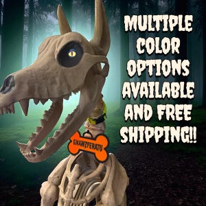 May include: A beige skeletal dog figure with a yellow collar and an orange bone-shaped tag featuring the text GNAWZFERATU. The image includes the text MULTIPLE COLOR OPTIONS AVAILABLE AND FREE SHIPPING!! against a dark forest background.