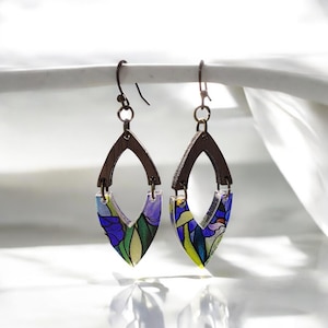 May include: A pair of dangle earrings with a stained glass design. The earrings feature a dark brown, open teardrop shape with a colorful floral pattern in shades of blue, green, and yellow. The earrings hang from a simple hook.