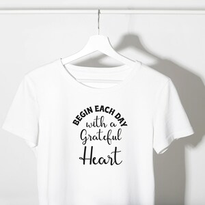 May include: White t-shirt with black text that reads "Begin each day with a grateful heart".