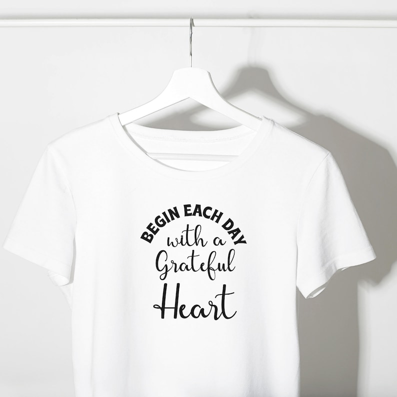 May include: White t-shirt with black text that reads "Begin each day with a grateful heart".