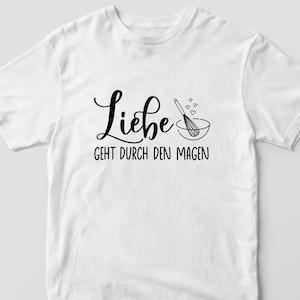 May include: White t-shirt with black text that reads "Liebe geht durch den Magen" which translates to "Love goes through the stomach". A black whisk and bowl are pictured above the text.