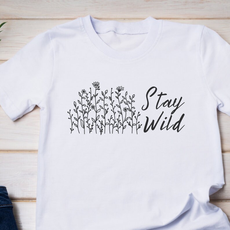 Op de afbeelding: Wit T-shirt met een zwart bloemenontwerp en de tekst "Stay Wild" gedrukt op de voorkant.