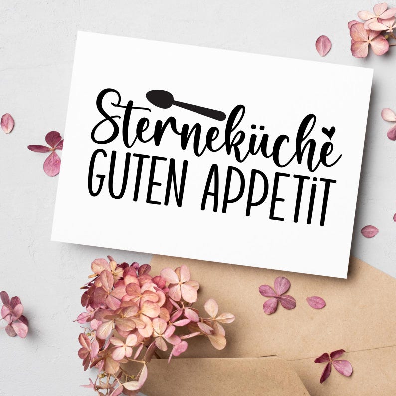 Op de afbeelding: Een witte kaart met de zwarte tekst "Sternek&uuml;che GUTEN APPETIT" en een lepelillustratie. De kaart is versierd met roze bloemen en een bruine envelop, wat een decoratieve uitstraling cre&euml;ert.
