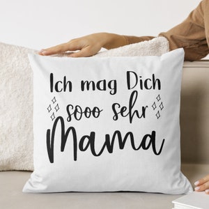 Pu&ograve; includere: Un cuscino bianco con testo nero che dice "Ich mag Dich sooo sehr Mama" con piccoli diamanti intorno al testo.