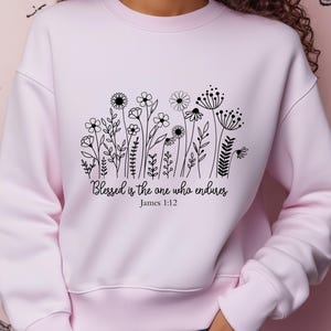 May include: Pink sweatshirt with a black floral design and the text "Blessed is the one who endures, James 1:12".