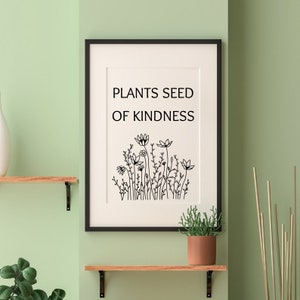 Op de afbeelding: Zwart-witte print met de tekst "Plants seed of kindness" en een tekening van een bloemenveld. De print is ingelijst in een zwart frame en hangt aan een lichtgroene muur.