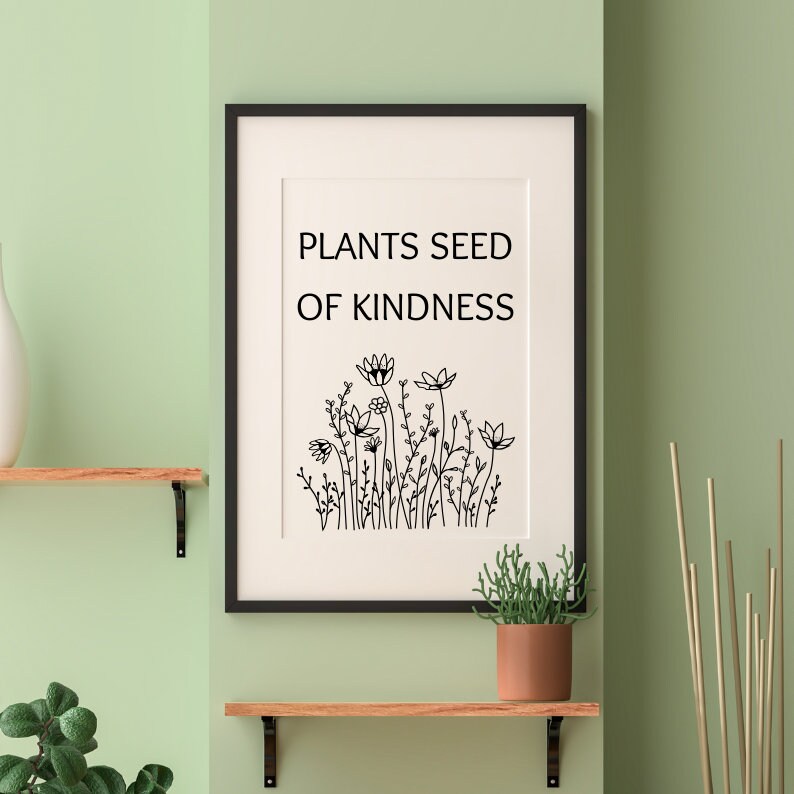 Op de afbeelding: Zwart-witte print met de tekst "Plants seed of kindness" en een tekening van een bloemenveld. De print is ingelijst in een zwart frame en hangt aan een lichtgroene muur.