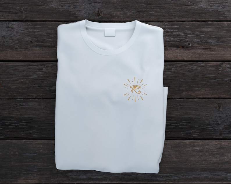 May include: White t-shirt with a gold eye of Horus graphic design on the front.