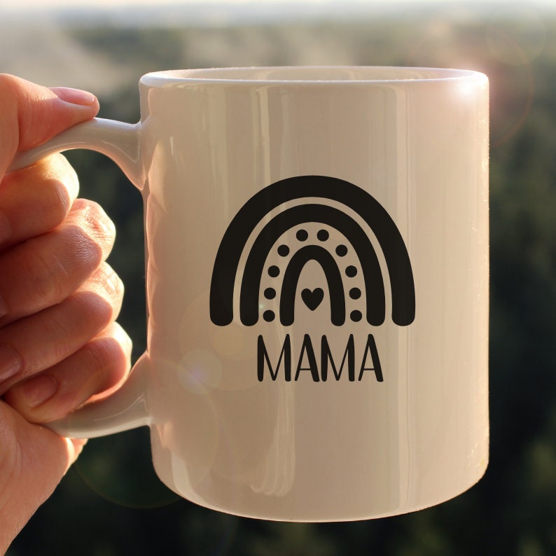 Pu&ograve; includere: Una tazza in ceramica bianca con un design arcobaleno bianco e nero e la parola "MAMA" stampata sotto.