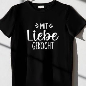 May include: Black t-shirt with white text that reads "MIT LIEBE GEKOCHT" which translates to "Cooked with love" in English.