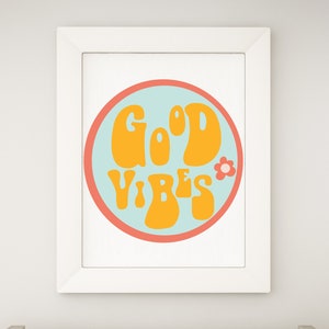 Puede incluir: Un estampado enmarcado con las palabras "GOOD VIBES" en naranja, con letras de estilo retro. El texto est&aacute; dentro de un c&iacute;rculo azul claro con un borde coral y un peque&ntilde;o gr&aacute;fico de flores. El marco es blanco.