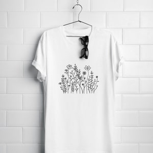 May include: White t-shirt with a black line drawing of a cluster of flowers and leaves.