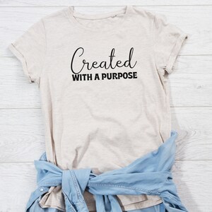 May include: A beige t-shirt with the text "Created with a purpose" in black lettering.