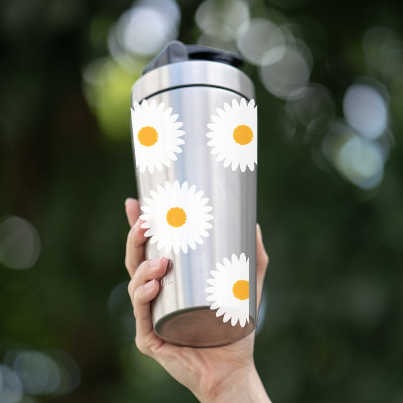 May include: A stainless steel water bottle with a white daisy pattern. The bottle has a screw-on lid and is held in a person's hand.