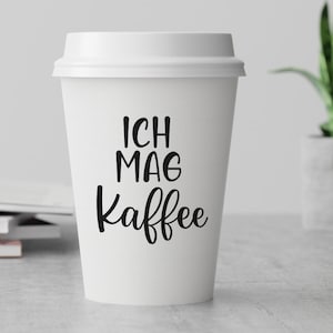 May include: White to-go coffee cup with black text that reads "Ich mag Kaffee" which translates to "I like coffee" in English.